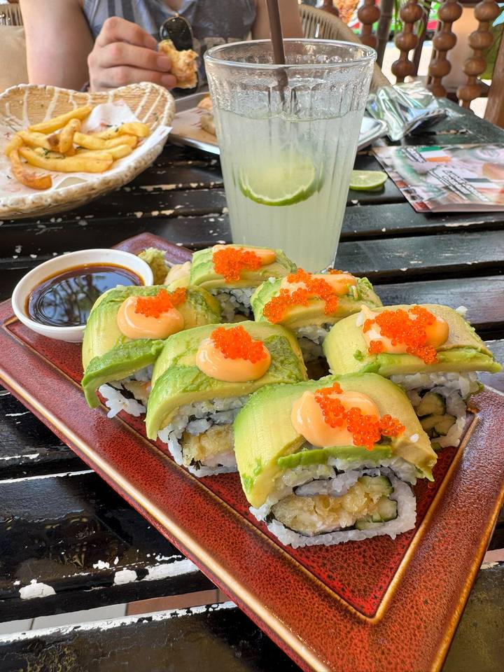 A plate of avocado-topped sushi rolls garnished with orange roe, served with soy sauce.