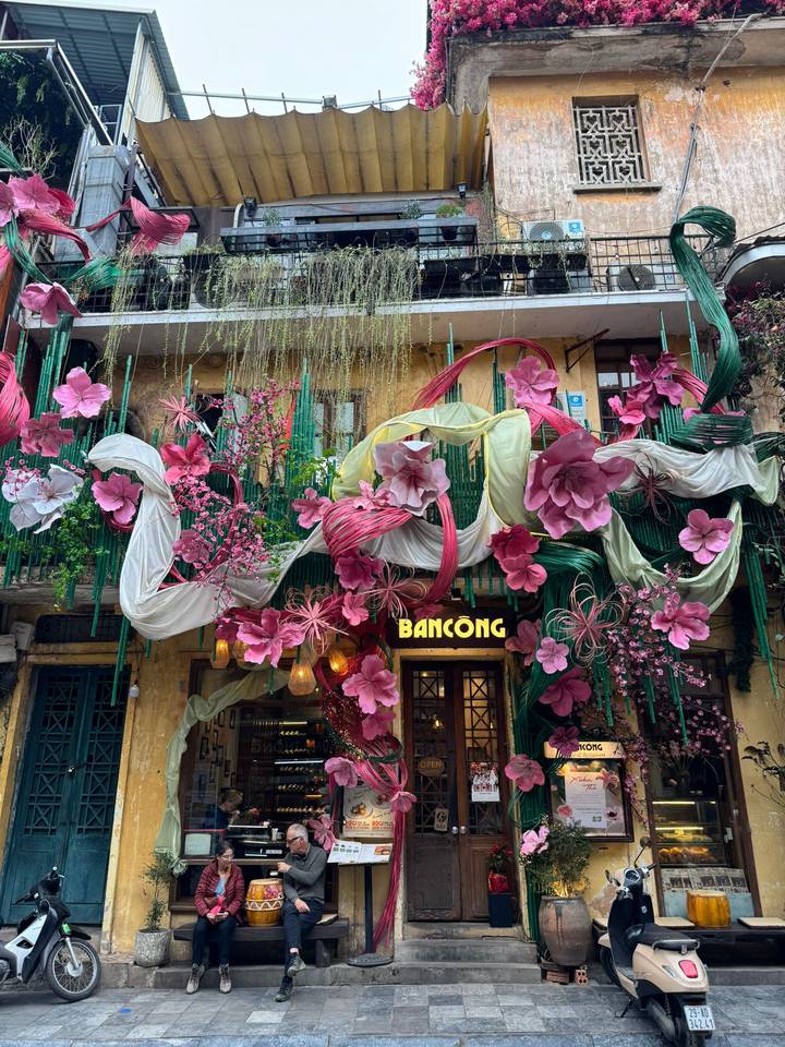 Colorful storefront adorned with oversized pink floral decorations and flowing fabric.