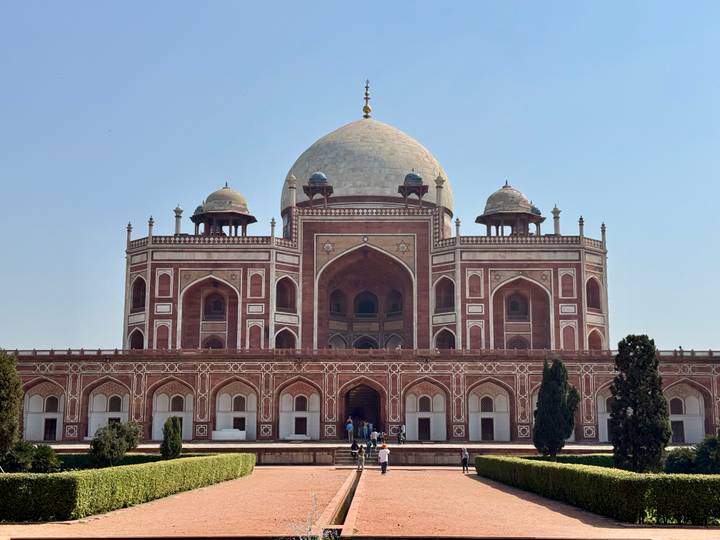 The symmetrical façade of Humayun's Tomb with visitors on the steps under a clear sky.