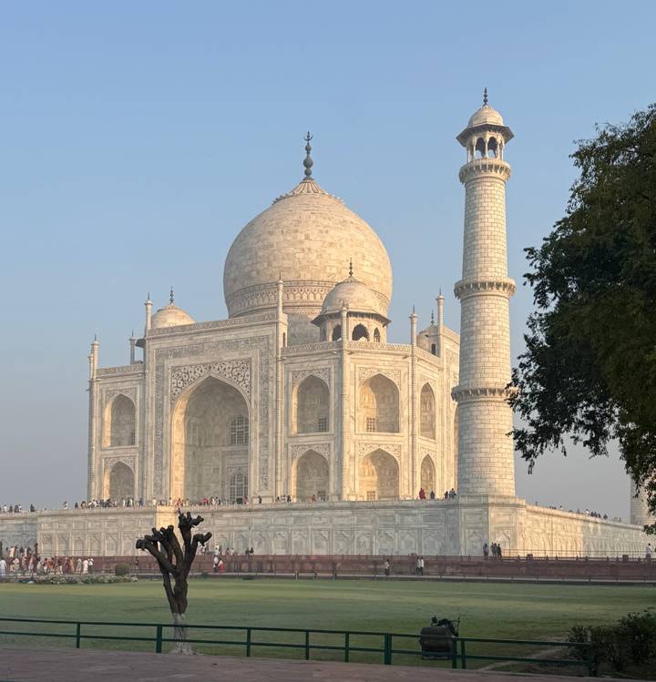 The Taj Mahal glowing in soft light with crowds walking along the platform.