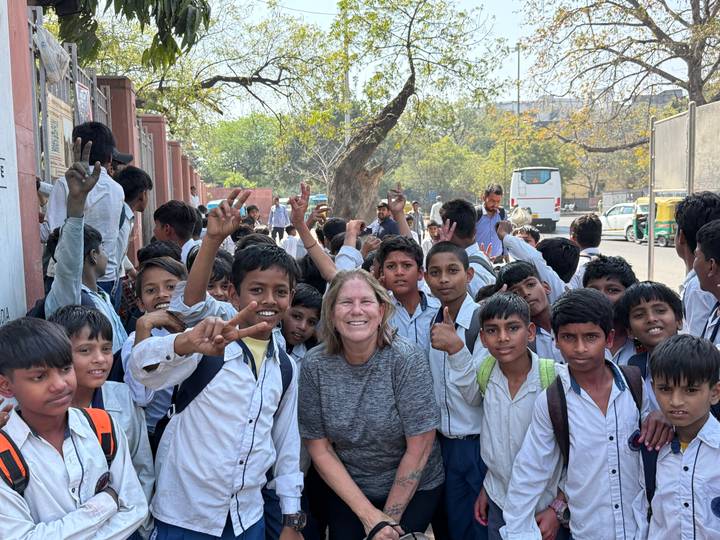 Smiling traveller surrounded by a large group of schoolchildren posing on a street.