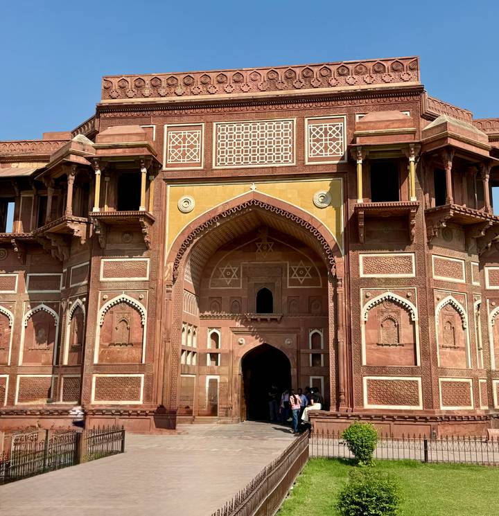 Ornate red-stone gateway with intricate carvings and people entering through the arch.