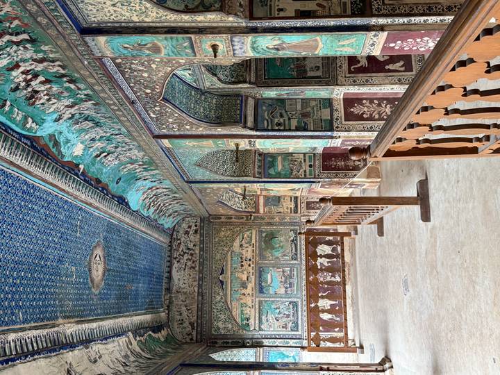 Vibrantly painted corridor with detailed blue ceilings and frescoed walls in a historic palace.