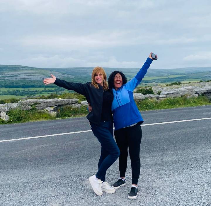 Two happy friends pose with outstretched arms beside an Irish countryside road.