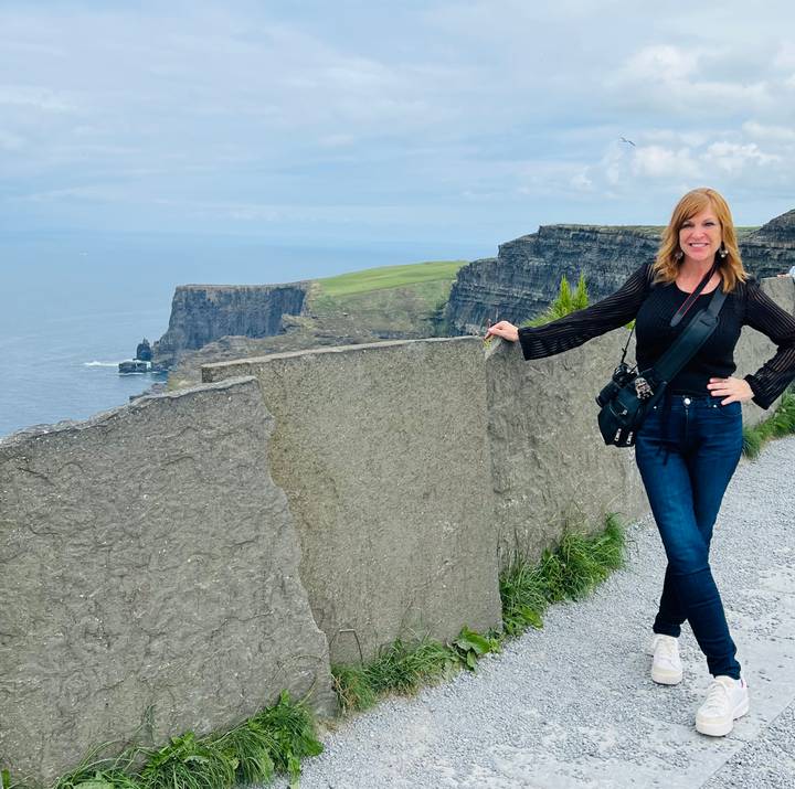Traveler smiles beside the towering Cliffs of Moher overlooking the Atlantic.