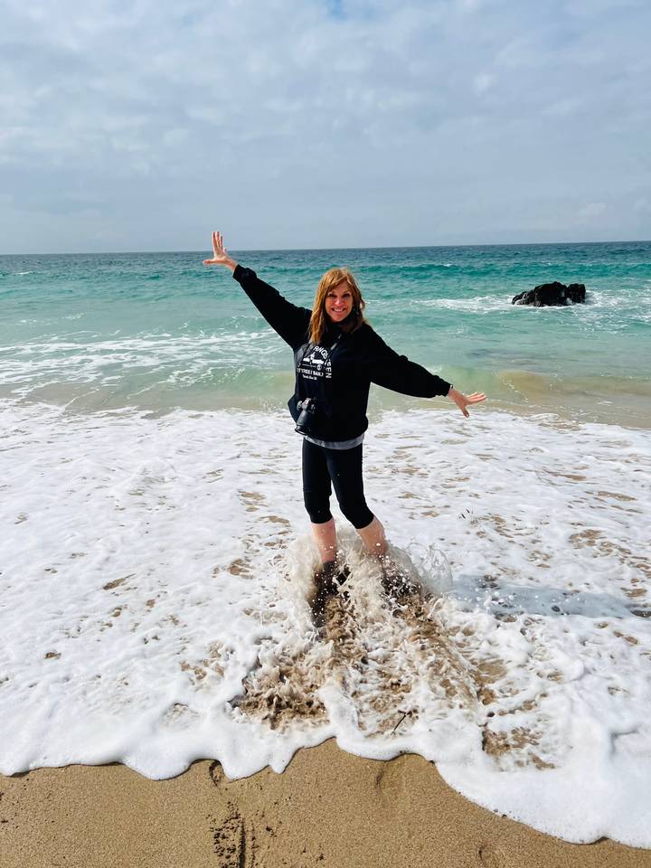 Woman splashes joyfully in shallow turquoise surf on a sandy beach.