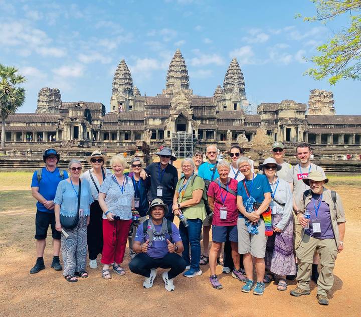 Smiling tour group posing in front of the ancient towers of Angkor Wat on a sunny morning.