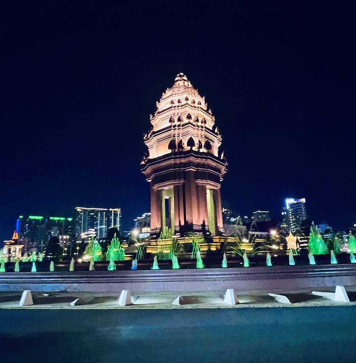 Independence Monument in Phnom Penh dramatically lit at night with neon-colored fountains in the foreground.