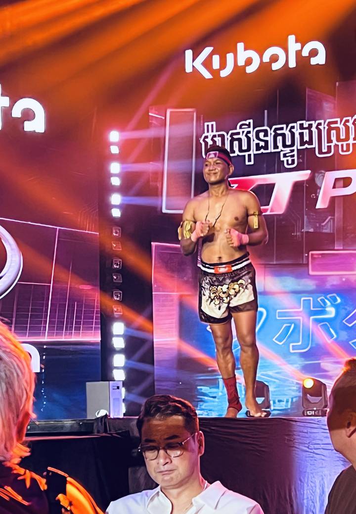Muay Thai fighter on a brightly lit stage during an evening boxing show.