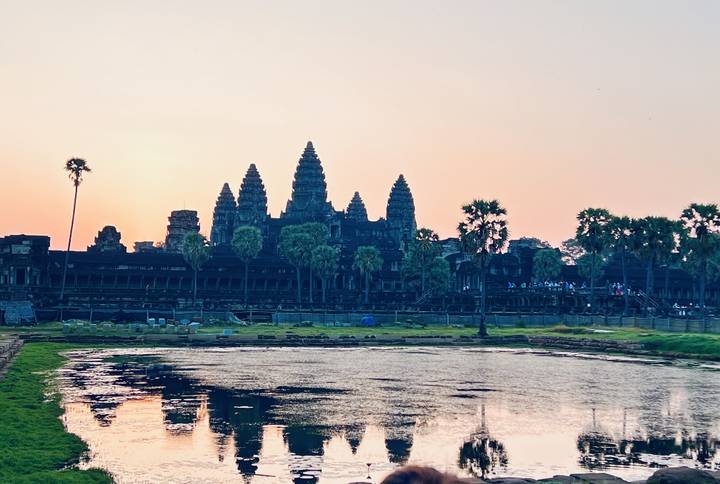 Silhouette of Angkor Wat’s spires reflected in a pond at soft pink sunrise.