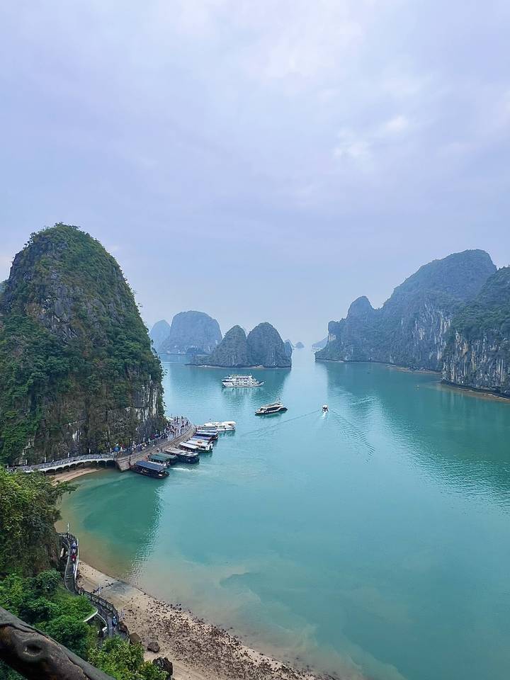 Emerald waters, limestone karsts and cruising boats in the misty expanse of Halong Bay.