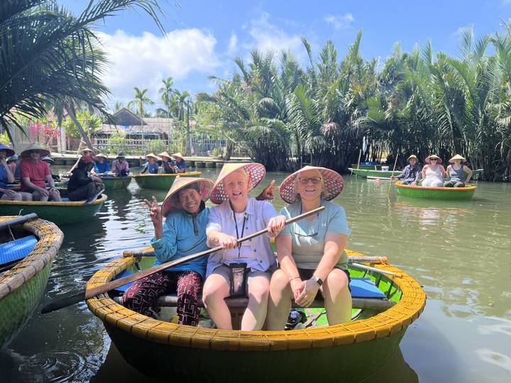 Travelers wearing conical hats paddle circular basket boats through a lush coconut waterway near Hoi An.