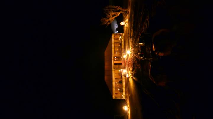 Distant desert camp tent illuminated by lanterns against dark night sky.