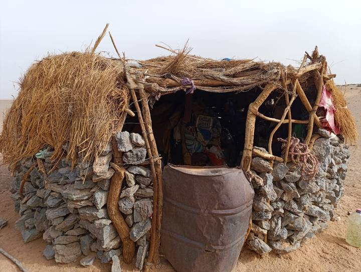 Simple stone and thatch desert hut with open doorway and rustic roof.