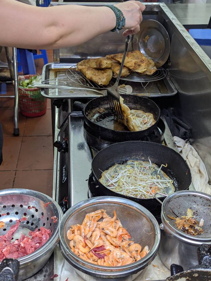 Street-food cook prepares sizzling pancakes in black pans with bean sprouts