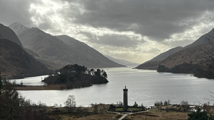 A moody Highlands panorama of Loch Shiel with the Glenfinnan Monument in the foreground and misty mountains beyond.