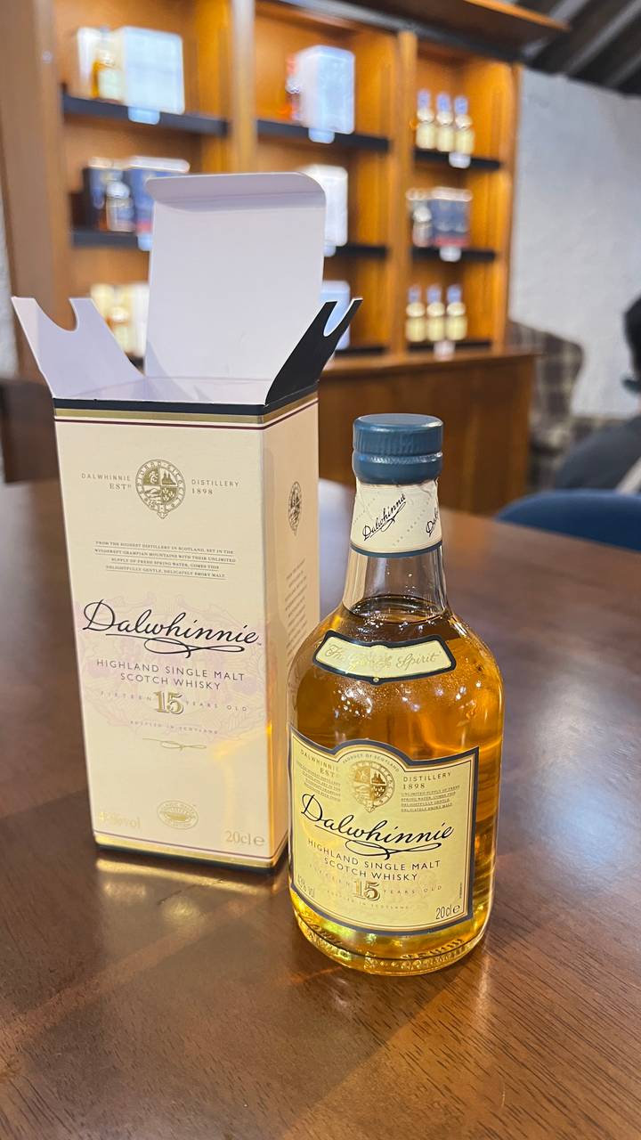 A close-up of a Dalwhinnie 15-year-old Highland single malt Scotch whisky bottle beside its presentation box on a wooden table.