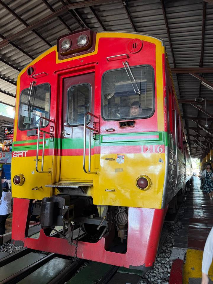 Front of colorful SRT train at station with driver visible through window.