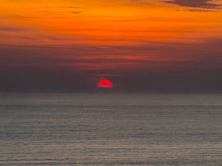 Vibrant red-orange sun setting over calm ocean horizon.