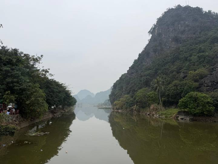 Calm river reflecting karst hills and hazy sky in Ninh Binh.