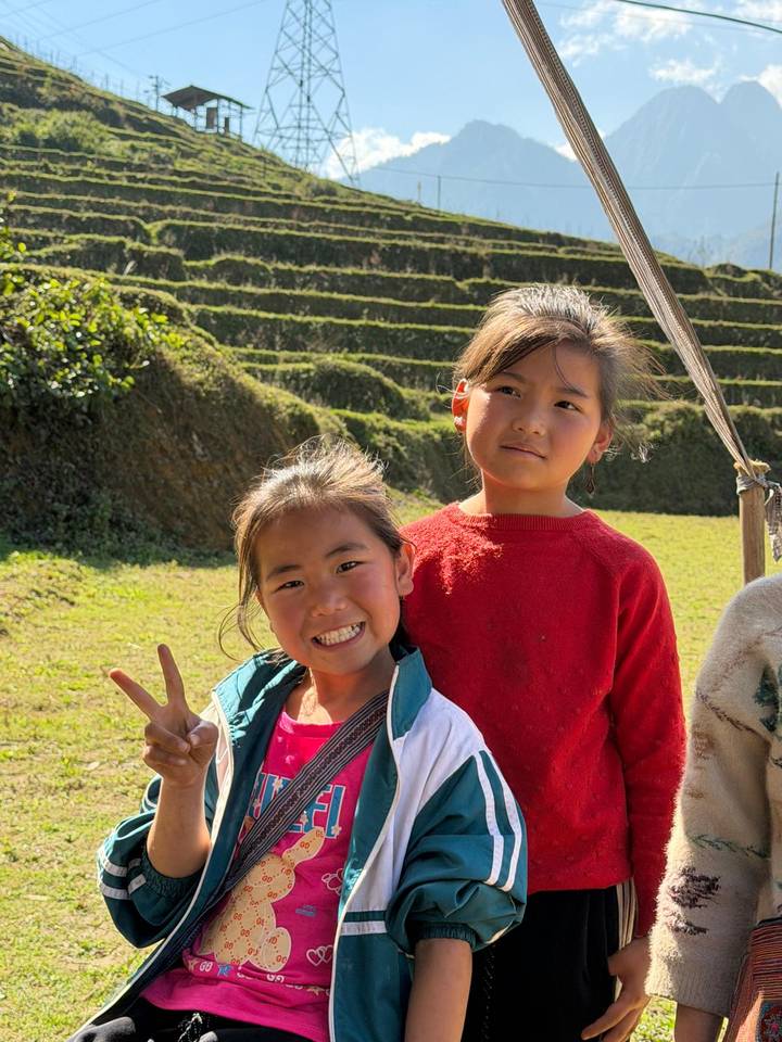 Two smiling local girls in terraced rice field region of Sapa, one flashing peace sign.