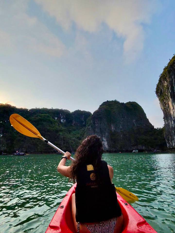 Person kayaking in emerald green waters surrounded by towering limestone cliffs at Halong Bay
