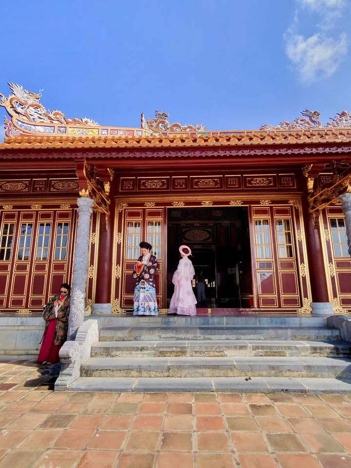 Visitors in traditional dress outside an ornate red and gold Vietnamese temple entrance