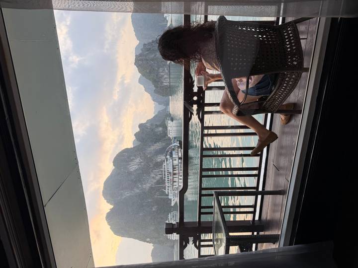 Woman relaxing with coffee on a cruise cabin balcony overlooking karst islands of Halong Bay at dawn