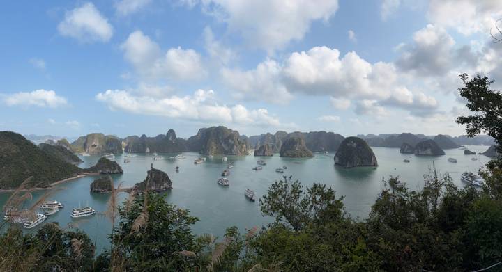 Panoramic view of Halong Bay with numerous cruise boats sailing among limestone islands under blue sky and fluffy clouds