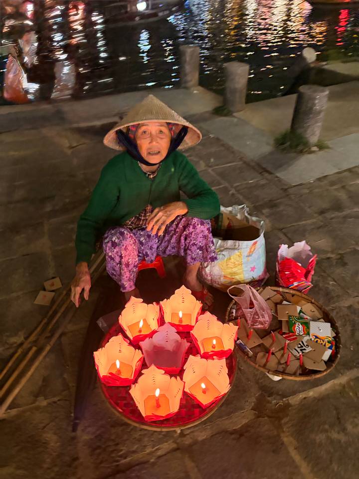 Street vendor in conical hat selling floating lanterns at night in Vietnam