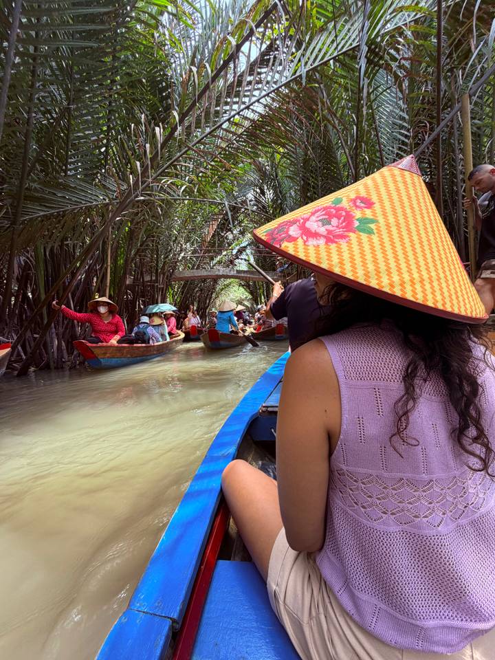 Tourists wearing conical hats paddling narrow boats through lush palm canals of the Mekong Delta