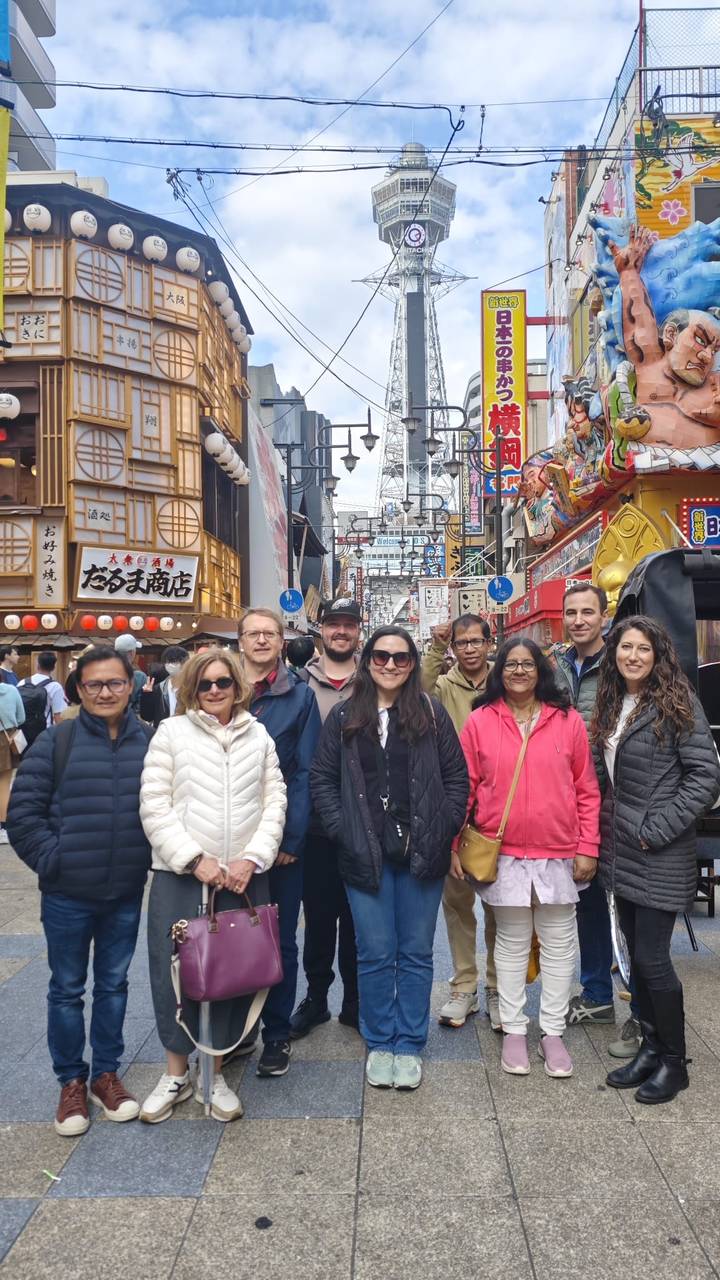 Tour group posing on a busy street of neon signs and food stalls in Osaka’s entertainment district.