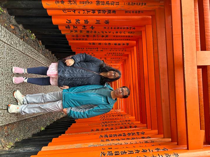 Two visitors stand among endless red torii gates at Kyoto’s Fushimi Inari shrine.