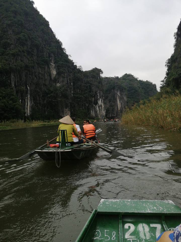 Rowboat with tourists in life jackets paddling through dramatic limestone cliffs and reeds