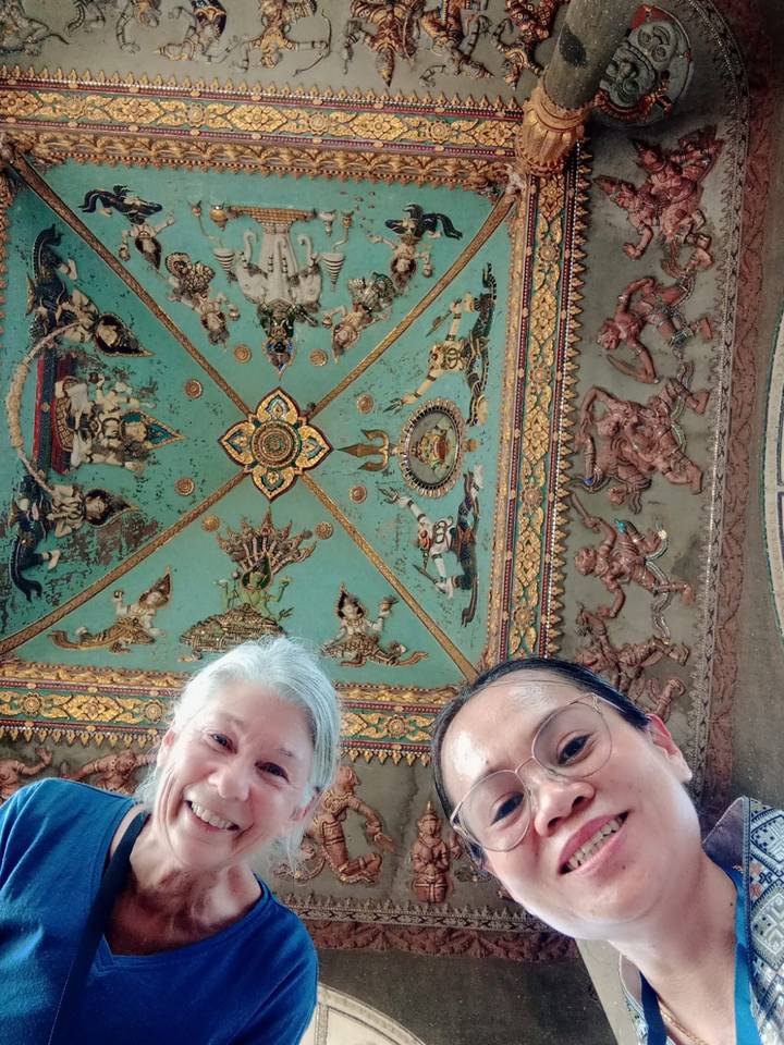 Two travellers’ selfie looking up at a richly painted temple ceiling with mythic figures.
