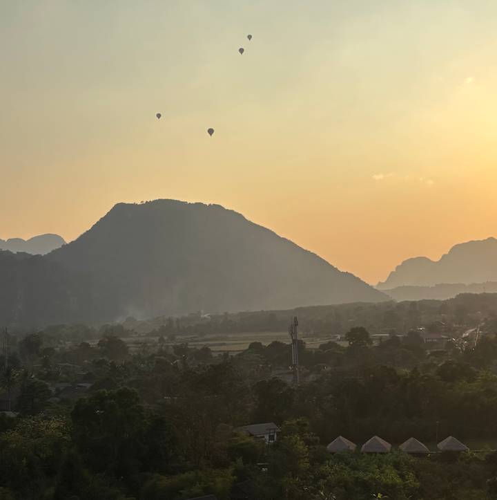 Silhouetted karst mountain and hot-air balloons over hazy valley at sunset.
