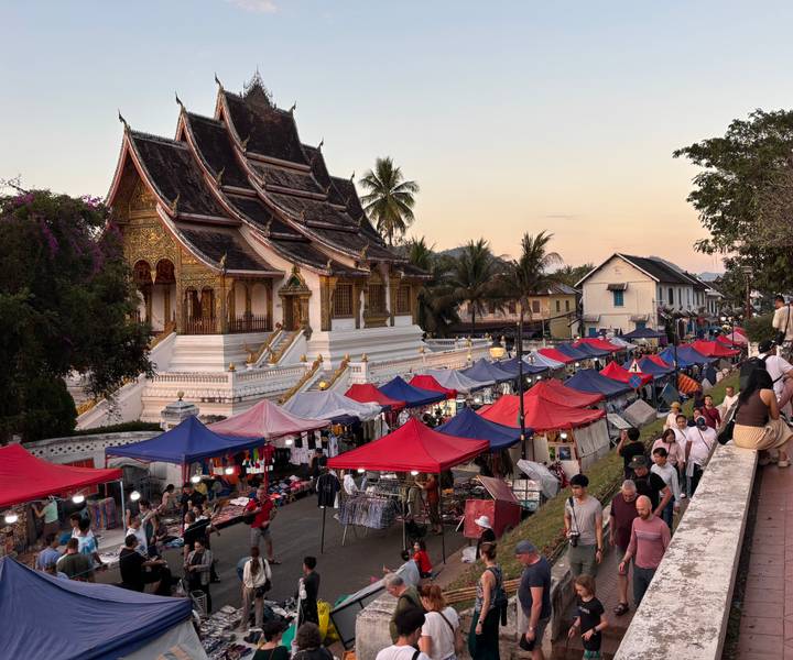 Evening market in Luang Prabang with red and blue canopies lining temple avenue.