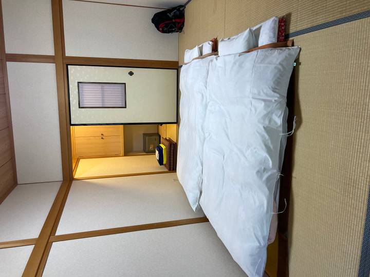 Simple tatami room with neatly laid out futon bedding beside a sliding shoji door.