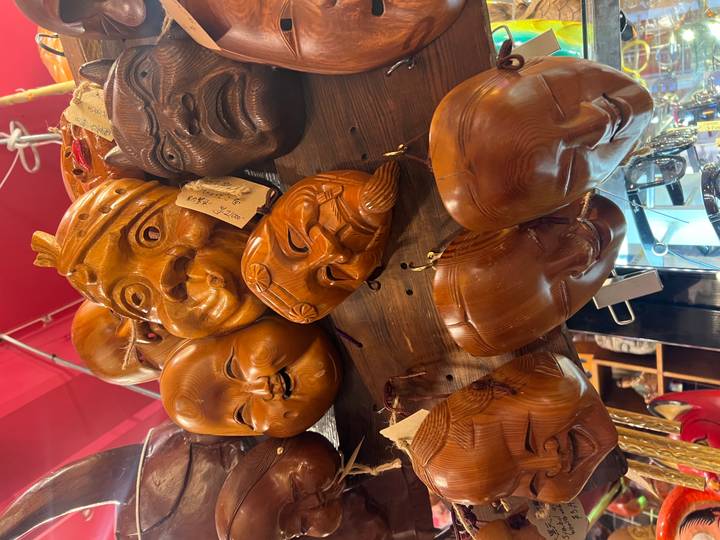 Cluster of carved wooden masks with expressive faces hanging in a market stall.