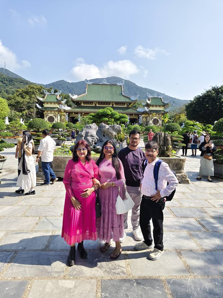 Family group posing in front of an ornate vihara and manicured gardens on a sunny day.