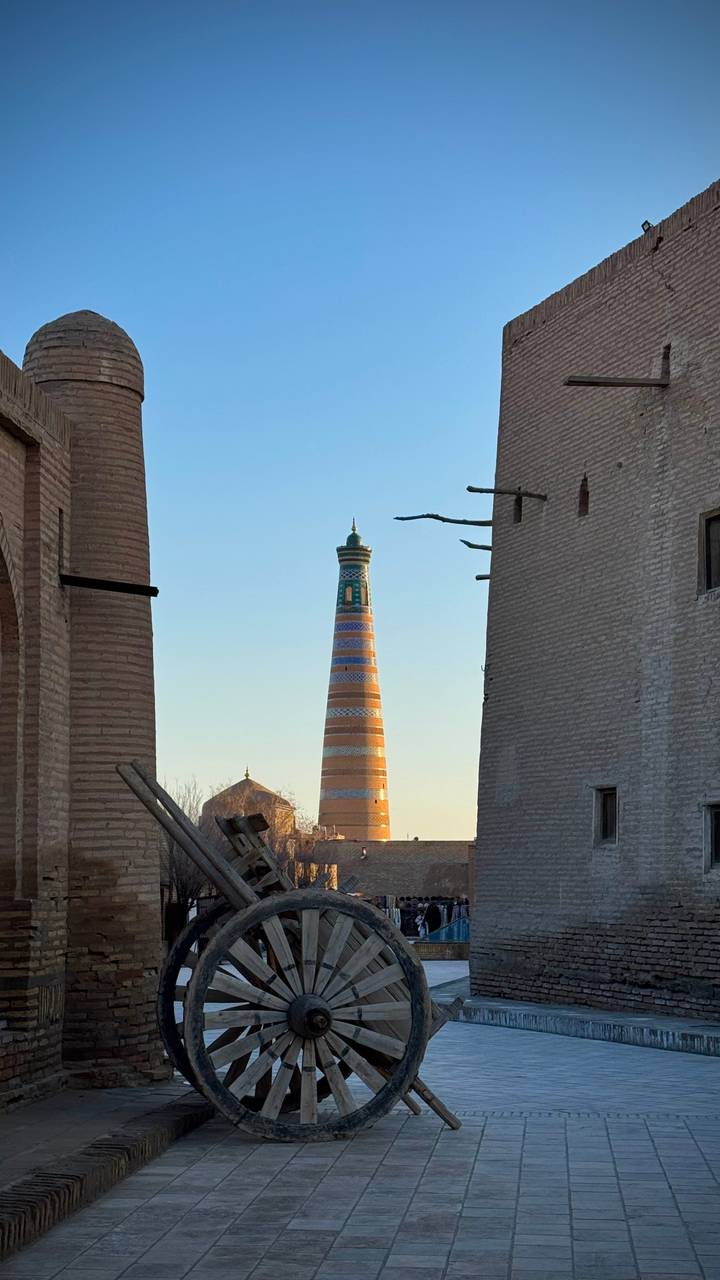 A tall, intricately tiled minaret rises between ancient brick buildings in warm afternoon light.