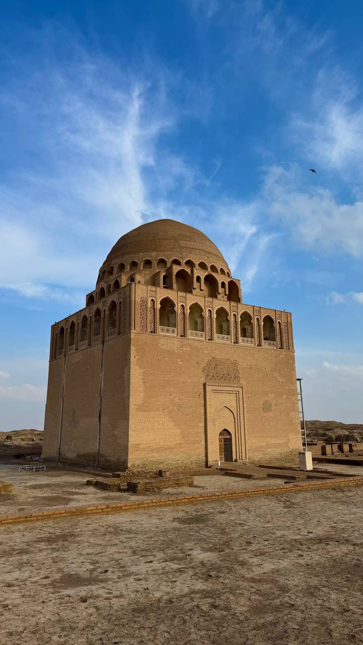 A massive square brick mausoleum with ornate arches stands against a bright blue sky.