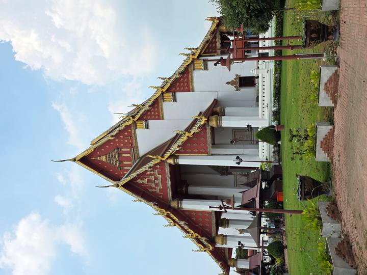 Grand red-white Viharn Phra Mongkol Bophit temple in Ayutthaya with ornate golden gables against a bright sky.