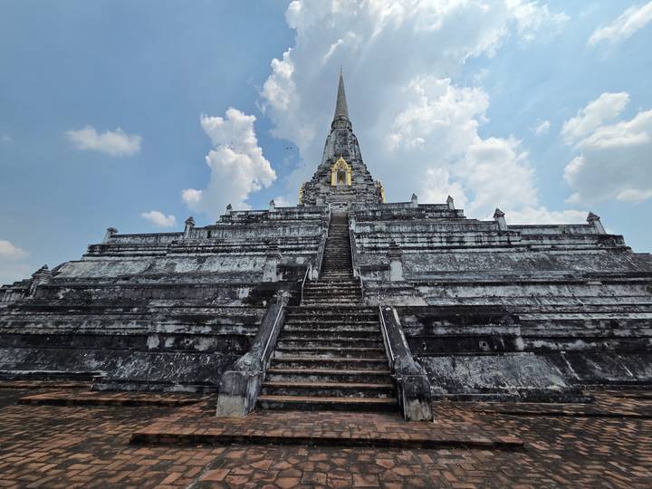 Massive grey-stone pyramid stupa with steep central stairway reaching toward a partly cloudy blue sky