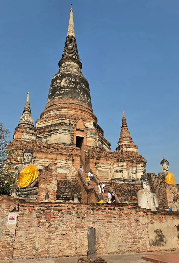 Close-up of Ayutthaya stupa base with weathered Buddha images and visitors climbing narrow staircase