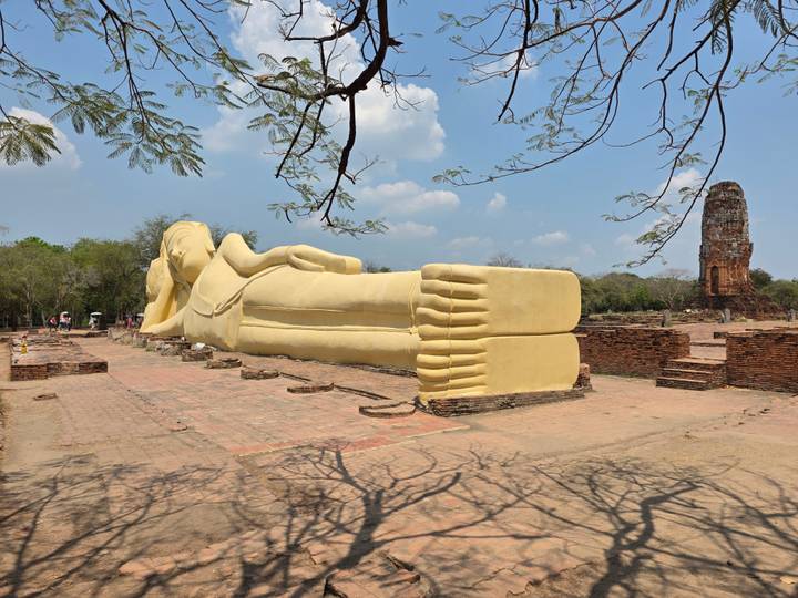 Large outdoor reclining Buddha coated in yellow placed amid ancient brick ruins under blue sky