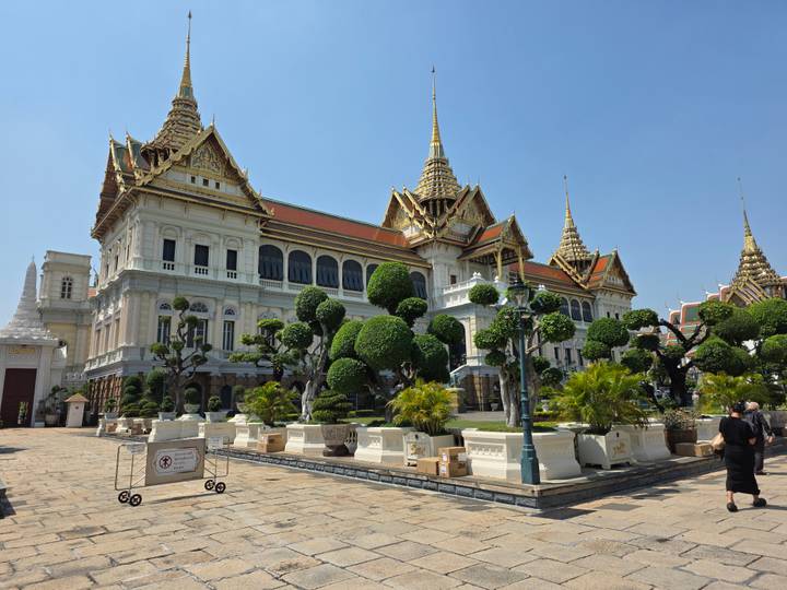 Elegant Grand Palace building with manicured topiary trees and gilded spires against clear blue sky