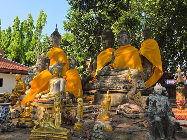 Row of ancient stone Buddha statues draped in bright orange cloth surrounded by smaller figurines and offerings