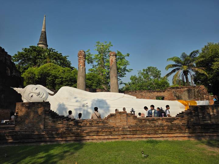 Large white reclining Buddha statue nestled within brick ruins with groups of visitors admiring the site