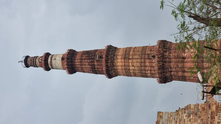 Tall red-sandstone minaret with successive balconies rising against an overcast sky